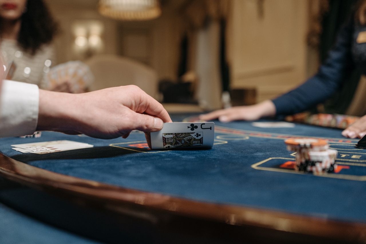 Guest lifting a playing card at a midnight-blue table with walnut edging
